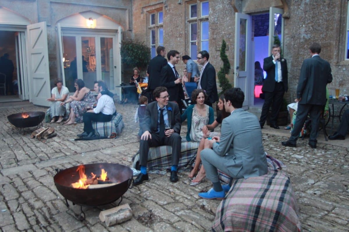 Guests gathered around fire pits in a courtyard at an evening wedding celebration