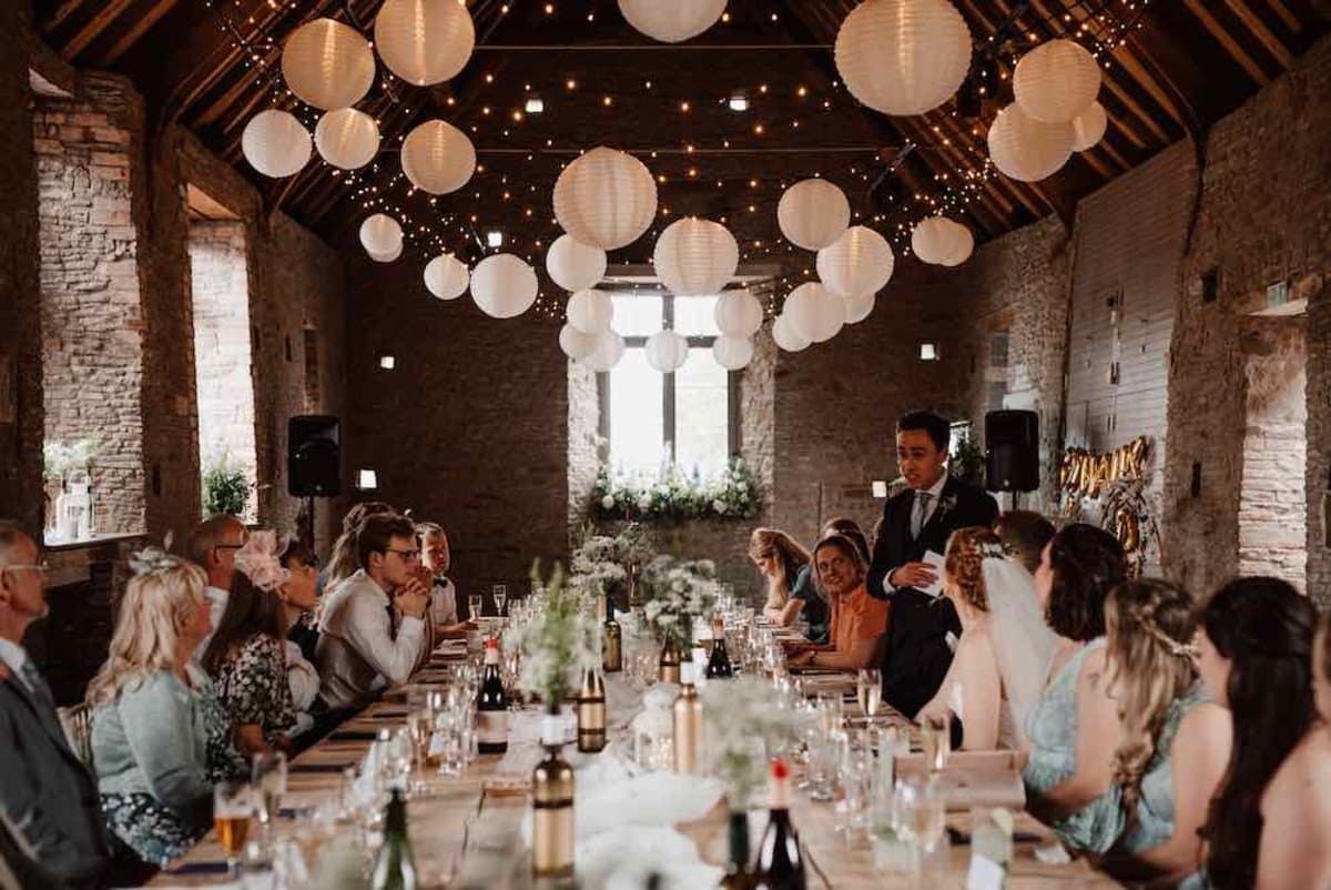 Wedding breakfast in a barn with fairy-light canopy, paper lanterns and long banquet tables