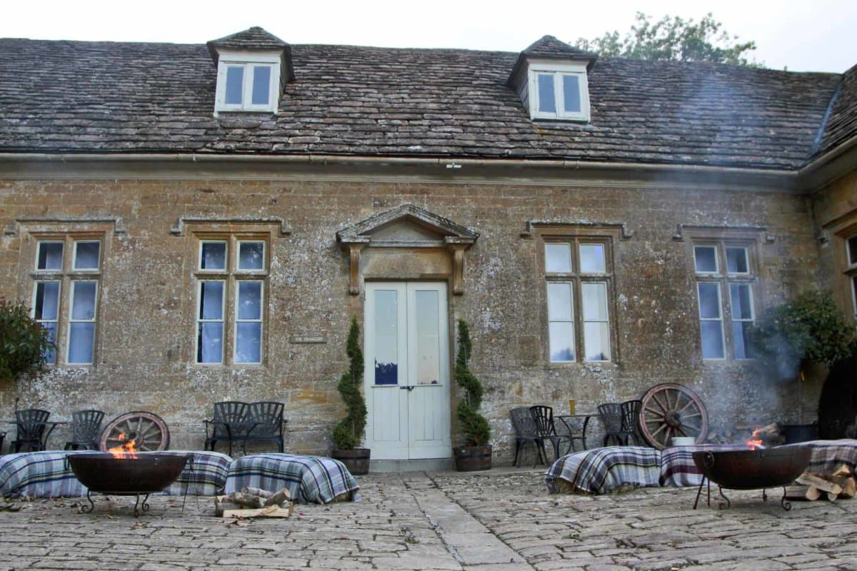 Fire pits outside a stone manor with hay-bale seating and plaid blankets
