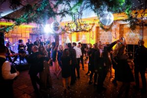 A party room with glitter-balls, mood lighting in Amber and people dancing to a band on a stage.