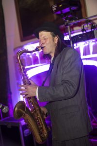A sa player blowing into his Sax, black hat and Pink fireplace also shown.