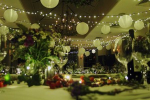 A fairy light canopy installed for a party at Babington House in Somerset. Lits of floritsry on tables, wine bottle and glasses and white shades hanging from the fairy-lights.