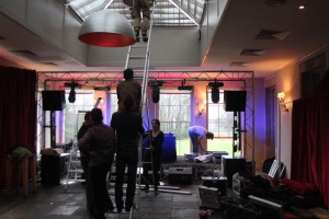 Rigging a party with riggers, ladder stage being built. A truss is above the stage with moving lights attached.