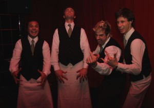 Four waiters in uniform making faces with a red background behnd.