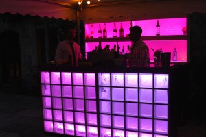 A cocktail bar and barmen at a private party with pink lighting on the fornt and rear of the bar to create a moody shote.