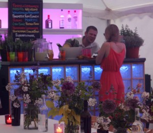 2 people talking at a coktail bar in a marquee with flowers in jars inthe foreground
