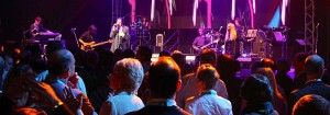 A large stage with live band in the background. In the foreground are a group of people staring at the stage.