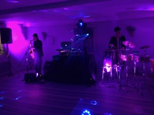 Moody shot with pink and purple lighting of a DJ setup with sax player to the left and percussionist to the right.DJ, Sax, Tresanton Hotel