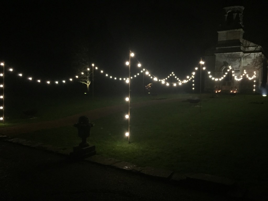Image of string lights at Babington House running up to the entrance of the church for a winter wedding.