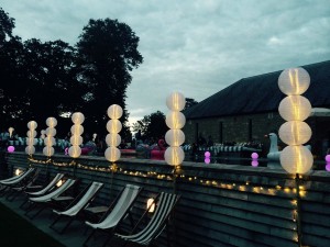 Babington House Swimming Pool with party lighting installed around the edge of the pool at dusk with inflatables and stripey furniture in the background.