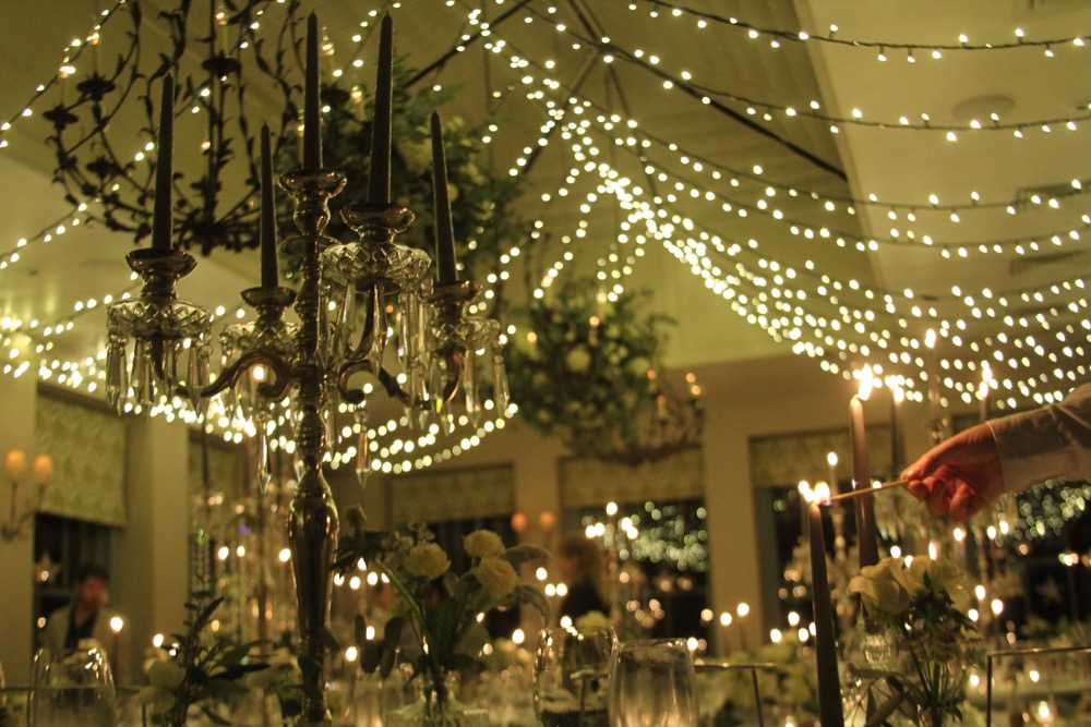 A Babington House Wedding breakfast. Lots of candles, and fairy-lights with a hand lihgting a candle