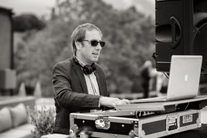 Black & White shot of a DJ playing outside with dark glasses and hands on a laptop