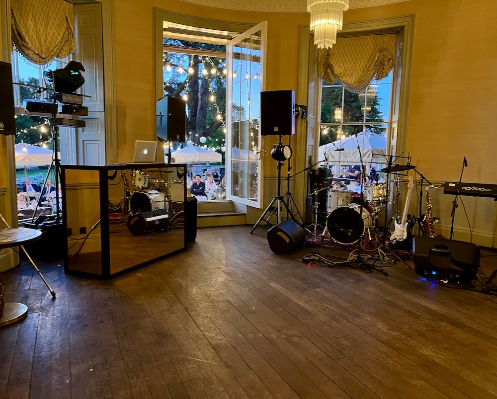 Interior, bar, dusk, dj setup on left, drum kit on right, large door open to people seated.
