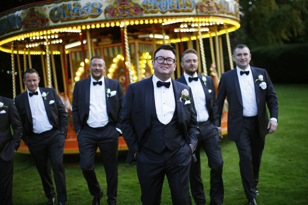 Five men in black tuxedos in front of Kkids carousel on a croquet lanwn.