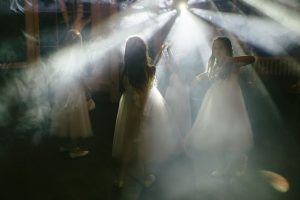 Four, young brides-maids in white dress in a dark bar. White beams of light silhouette the girls.
