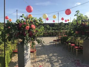 Daytime, walled garden in the summer, gold chairs and red pads, coloured shades suspended from a canopy.