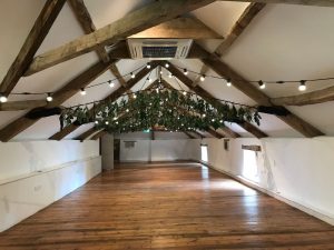 Large barn dining room style building, wooden floor, white walls, wooden beams, festoon lighting with fliage