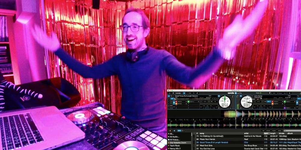 DJ with harsm open and large hands, dj decks shown, gold tassle curtain behind the DJ