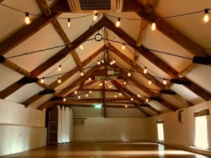Emty barn style room, wooden beams with a lighting canopy of edison vintage bulbs suspended from beams ina symetrical style.