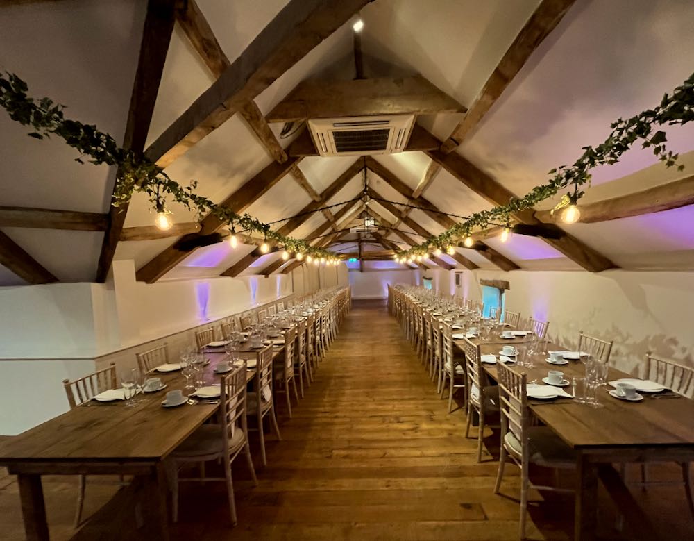 A long dining room, 2 trestle table runnign the lenghth with a string of festoon lighting above wrapped in ivy
