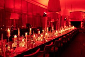 Party Lighting at Babington House, Somerset for the film Saltburn showing a long table filled with candles with Red lighting flooding the room,